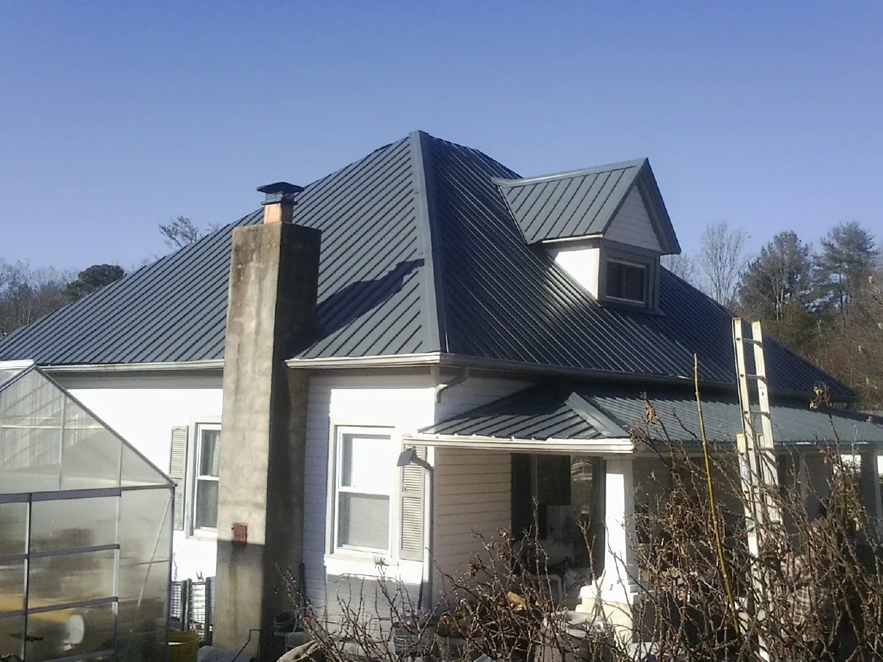 Dark blue standing seam metal roof on a white farmhouse with dormer — Slate & Tile Roof Repair by Roofing Brothers in Lynn Haven
