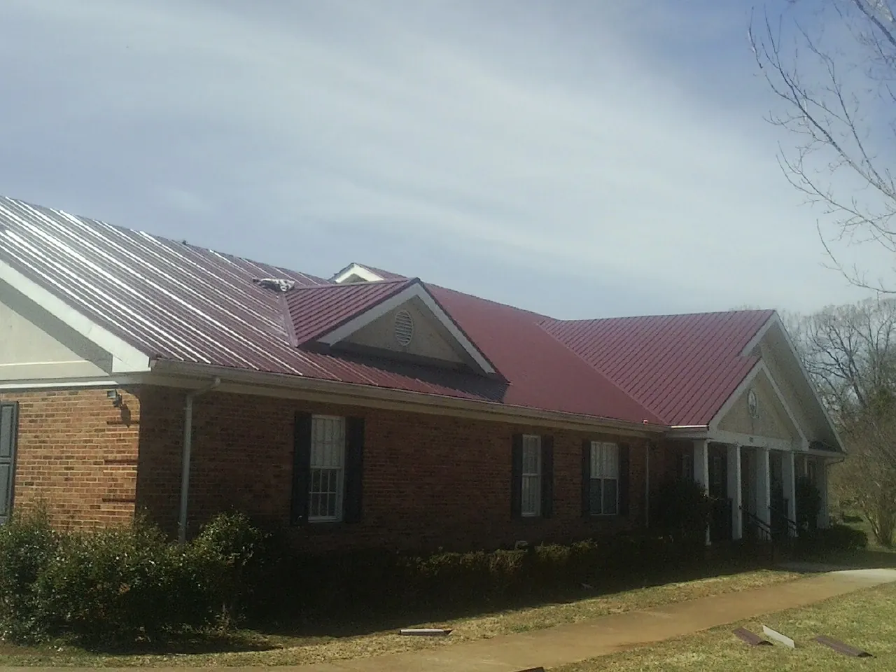 Red metal roof with gabled entries on a long brick building, from a Hail Damage Roof Repair job in Lynn Haven