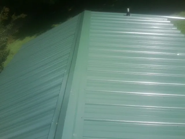 New green metal panels meeting at the ridge of a roof — Flat Roof Repair work by our crew in Lynn Haven