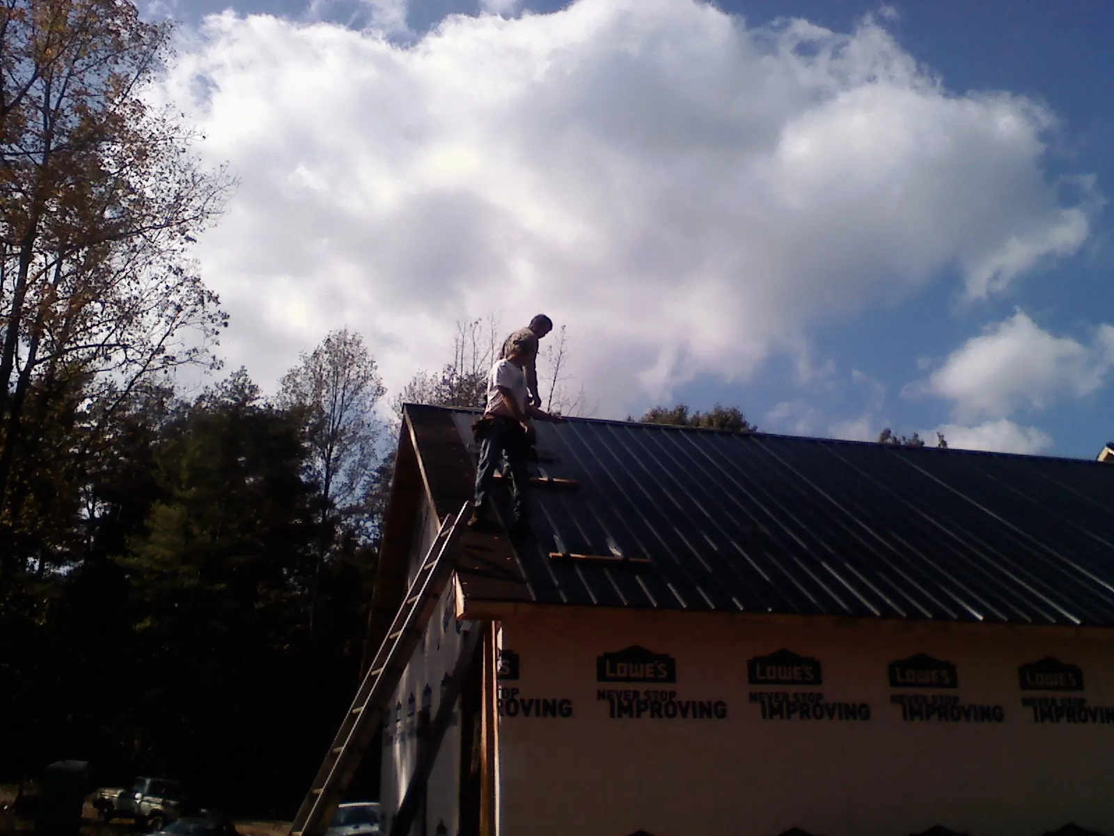 Roofer fastening dark metal panels high against a cloudy sky, from a Roof Inspection job in Lynn Haven