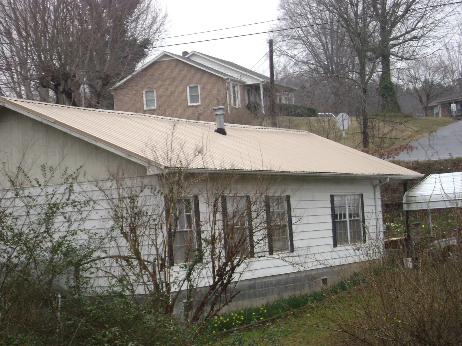 Tan metal roof on a white sided house set into a hillside — Commercial Roofing by Roofing Brothers in Lynn Haven