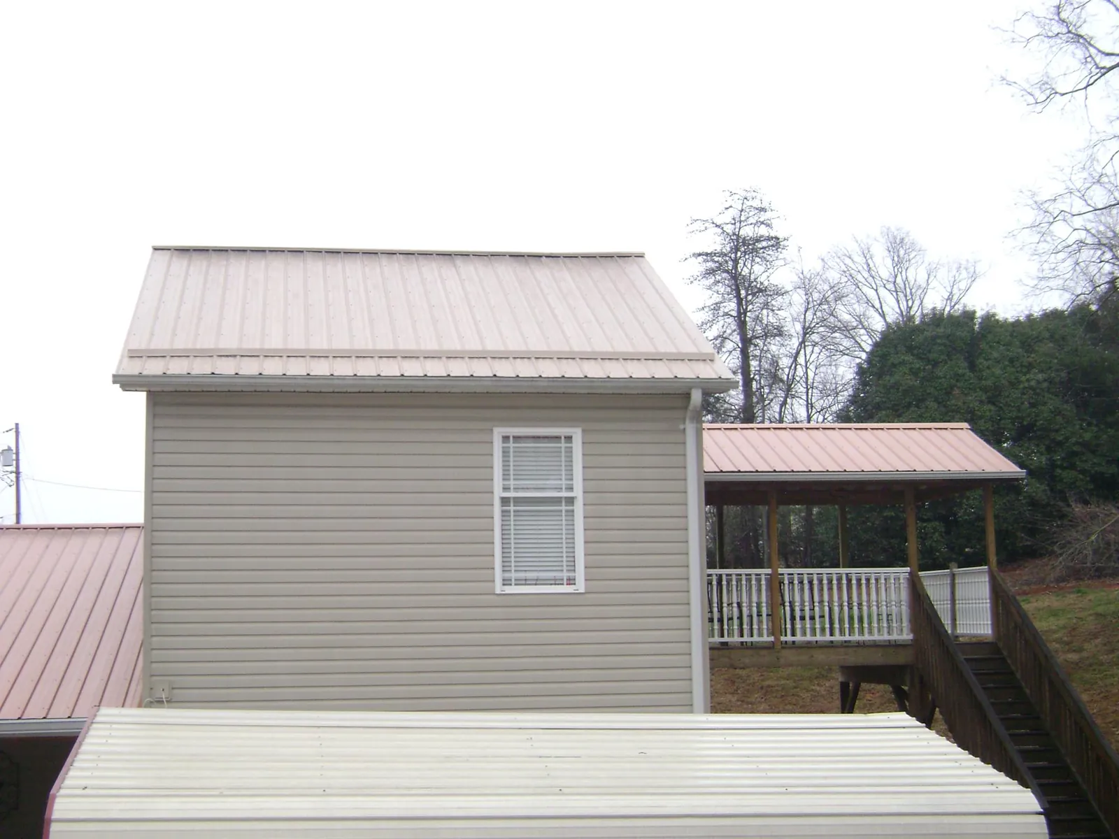 Tan metal roofs on a two story addition and attached porch, from a Roof Replacement job in Lynn Haven