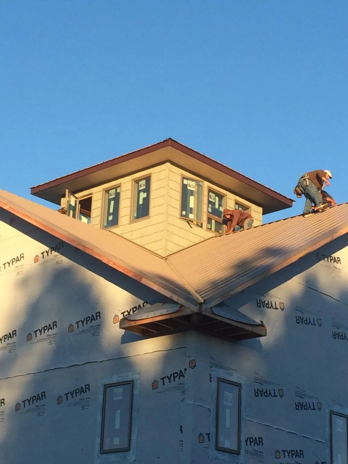 Roofers working around a rooftop cupola on a new metal roof at sunset — Roof Waterproofing in Lynn Haven by Roofing Brothers